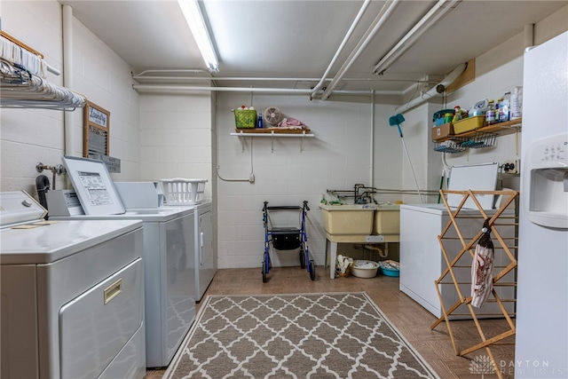 washroom with a sink, washing machine and clothes dryer, and concrete block wall