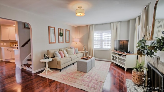 living area featuring baseboards, arched walkways, a fireplace with flush hearth, stairway, and dark wood-type flooring