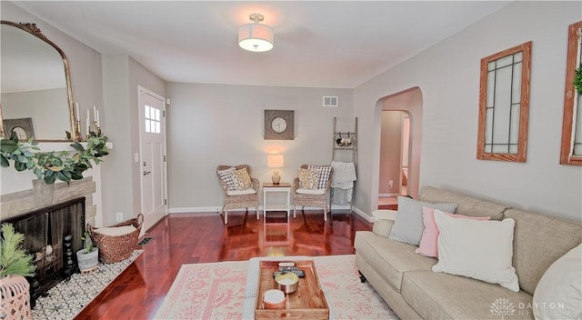 living area with dark wood-style floors, arched walkways, visible vents, a fireplace with flush hearth, and baseboards