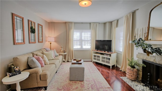 living room featuring a stone fireplace, dark wood-type flooring, and baseboards