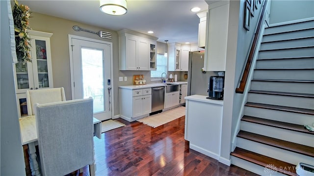 kitchen with white cabinets, glass insert cabinets, dark wood-style flooring, stainless steel appliances, and light countertops