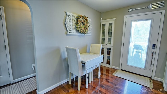 doorway with arched walkways, dark wood finished floors, and baseboards