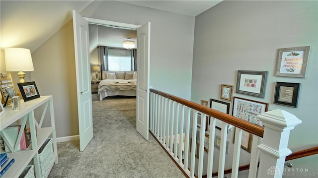 corridor with light carpet, vaulted ceiling, and an upstairs landing