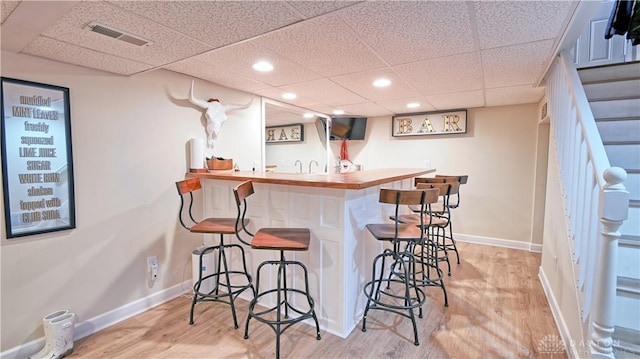 bar featuring baseboards, visible vents, light wood-style flooring, stairs, and indoor wet bar