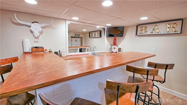 bar with baseboards, wood finished floors, a paneled ceiling, indoor wet bar, and recessed lighting