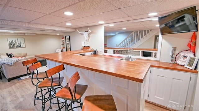 bar featuring light wood finished floors, stairway, indoor wet bar, and a sink