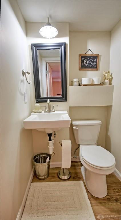 half bath with wood finished floors, toilet, and baseboards