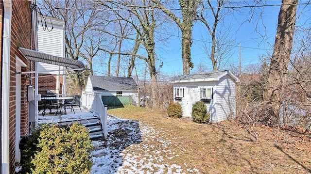 snowy yard featuring a wooden deck, fence, a storage unit, and an outbuilding