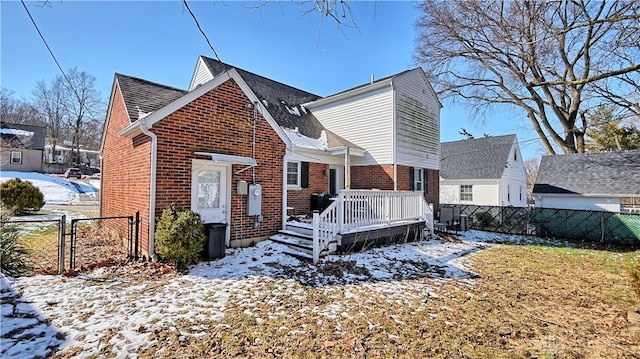 view of front of house featuring brick siding, fence, a wooden deck, and roof with shingles