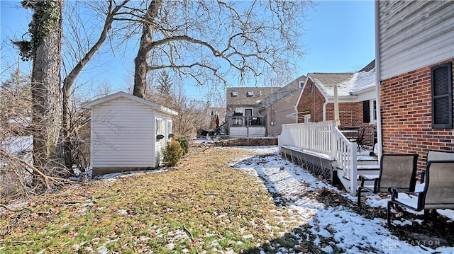 yard layered in snow featuring a deck, a shed, and an outbuilding