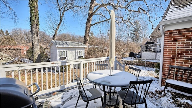 snow covered deck featuring an outbuilding, outdoor dining area, area for grilling, and a shed