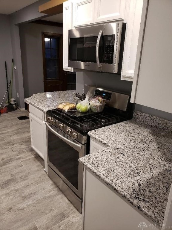 kitchen with stainless steel appliances, white cabinetry, light wood finished floors, and light stone counters