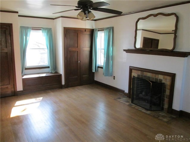 unfurnished living room with ornamental molding, baseboards, a tiled fireplace, and wood finished floors