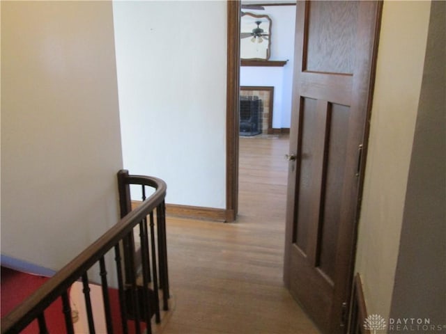 hallway featuring wood finished floors, an upstairs landing, and baseboards