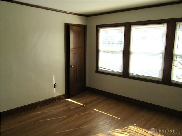 empty room with crown molding, baseboards, and dark wood-style flooring