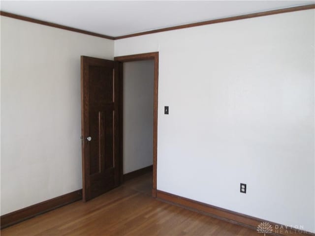 empty room featuring crown molding, dark wood finished floors, and baseboards