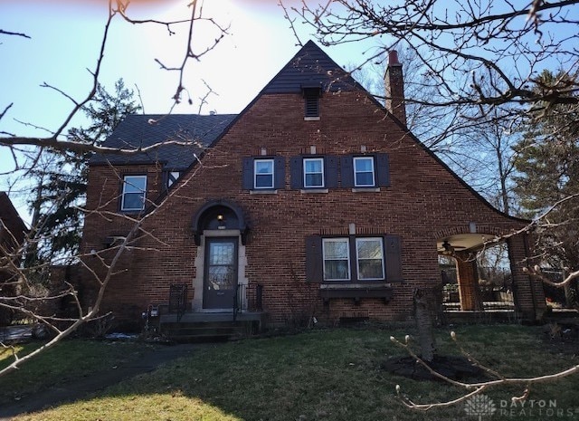 tudor house featuring brick siding, a lawn, and a chimney