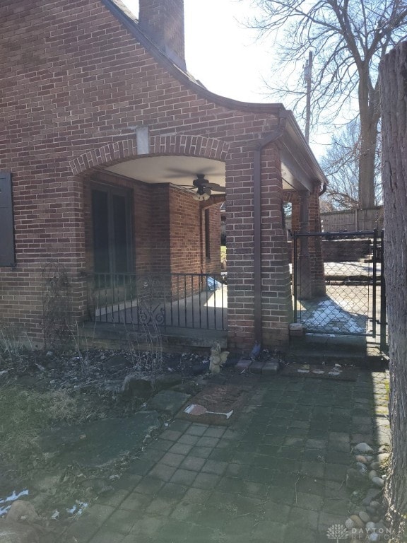 view of home's exterior featuring a chimney, a gate, a ceiling fan, and brick siding