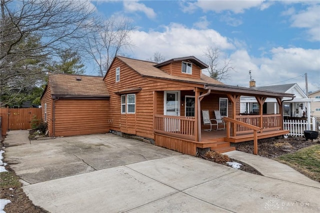 view of front of house featuring driveway, covered porch, and fence