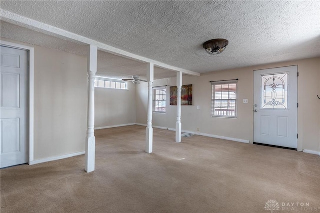 basement with a textured ceiling, baseboards, a ceiling fan, and light colored carpet