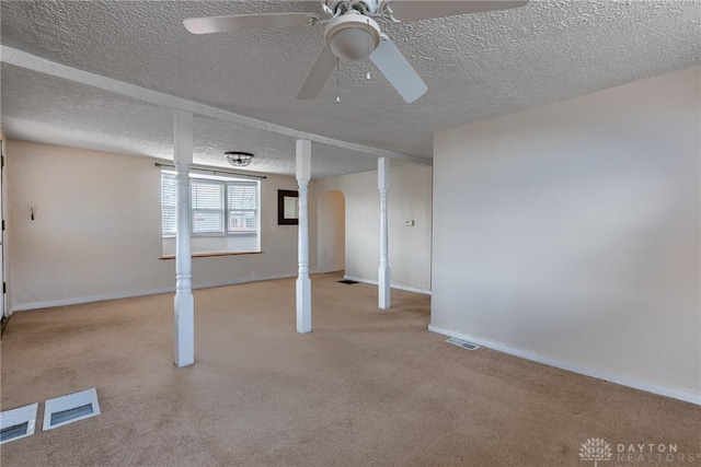 below grade area featuring visible vents, a ceiling fan, light carpet, a textured ceiling, and baseboards