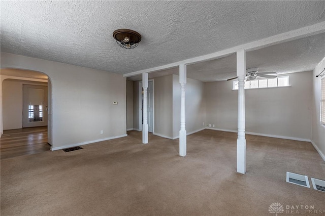 below grade area featuring arched walkways, carpet flooring, visible vents, and a ceiling fan