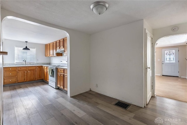 kitchen featuring electric range, visible vents, arched walkways, hanging light fixtures, and light countertops