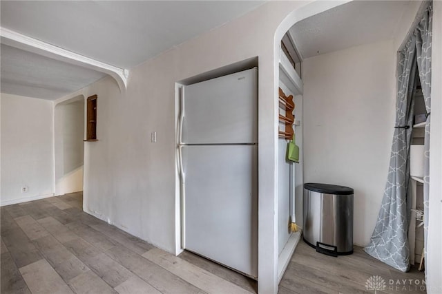 kitchen featuring light wood-style flooring, arched walkways, and freestanding refrigerator