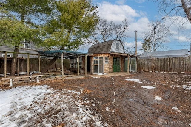 snow covered back of property with a shingled roof, fence, and a gambrel roof