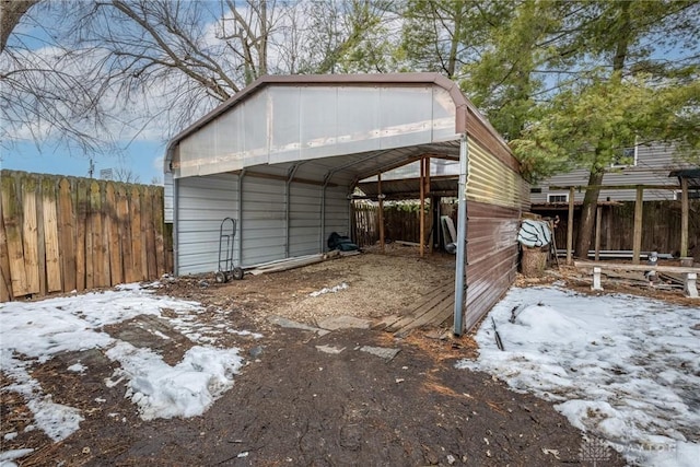 snow covered structure featuring driveway, fence, and a detached carport