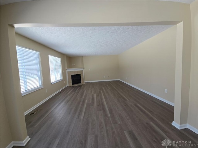 unfurnished living room featuring dark wood finished floors, visible vents, a tiled fireplace, a textured ceiling, and baseboards