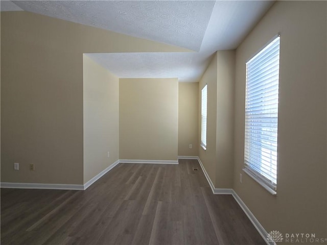 spare room featuring a textured ceiling, dark wood finished floors, and baseboards