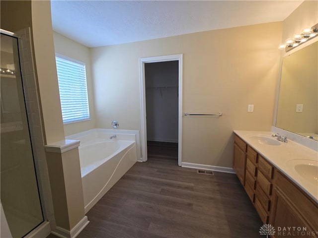 full bath featuring a garden tub, wood finished floors, a sink, visible vents, and a walk in closet