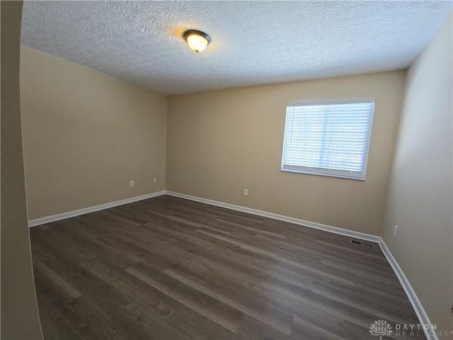 spare room with dark wood-type flooring, visible vents, a textured ceiling, and baseboards