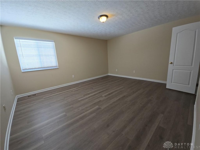 spare room featuring dark wood-style flooring, a textured ceiling, and baseboards