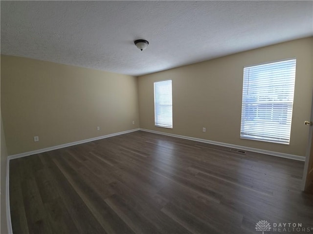 empty room featuring dark wood-style floors, visible vents, a textured ceiling, and baseboards