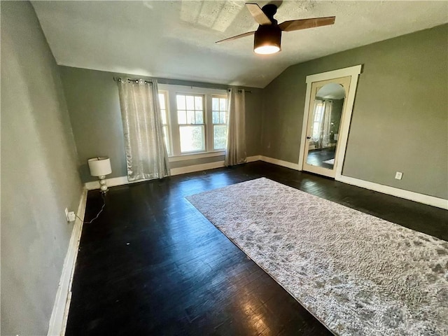 empty room featuring lofted ceiling, dark wood finished floors, a ceiling fan, and baseboards