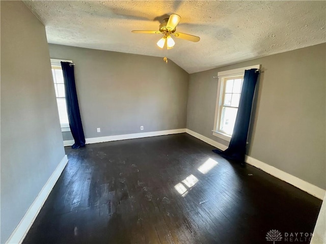 unfurnished room featuring lofted ceiling, dark wood-style flooring, a textured ceiling, and baseboards