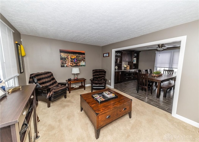 living area with light carpet, ceiling fan, a textured ceiling, and baseboards