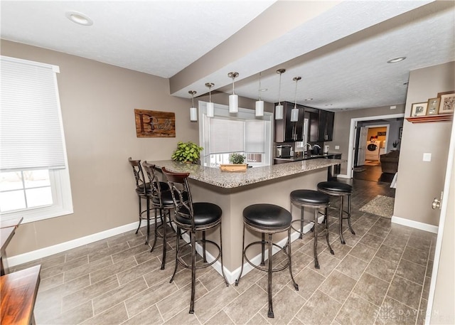 kitchen featuring baseboards, a peninsula, a kitchen breakfast bar, and light stone countertops