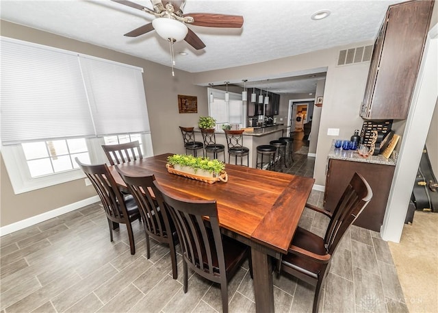 dining area with wood finish floors, visible vents, ceiling fan, a textured ceiling, and baseboards