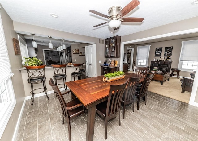 dining space featuring visible vents, baseboards, ceiling fan, a textured ceiling, and a bar