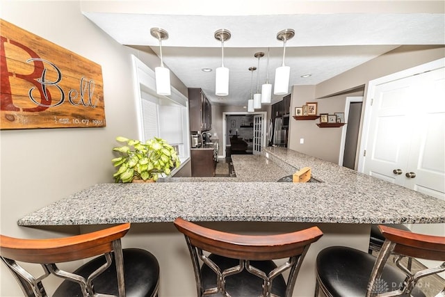 kitchen featuring pendant lighting, a peninsula, a kitchen bar, and light stone countertops