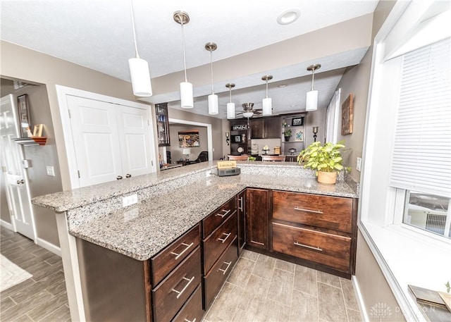 kitchen featuring dark brown cabinetry, baseboards, light stone counters, decorative light fixtures, and wood tiled floor