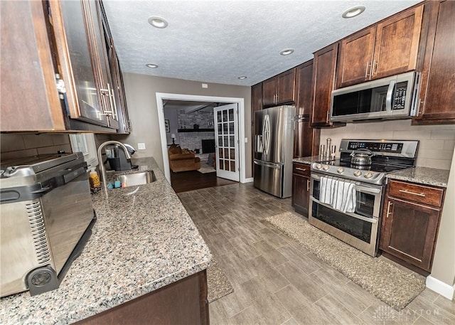 kitchen featuring a textured ceiling, light stone counters, a sink, appliances with stainless steel finishes, and backsplash