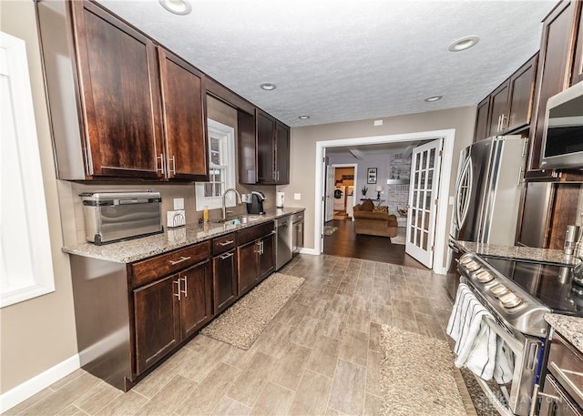 kitchen with light stone counters, appliances with stainless steel finishes, a sink, and dark brown cabinetry