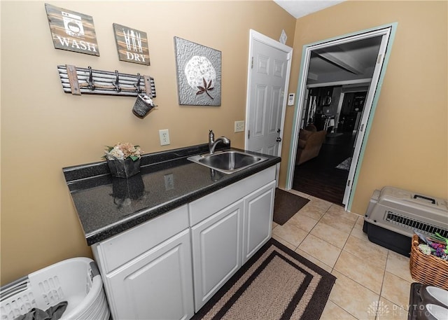 kitchen featuring dark countertops, light tile patterned flooring, a sink, and white cabinetry