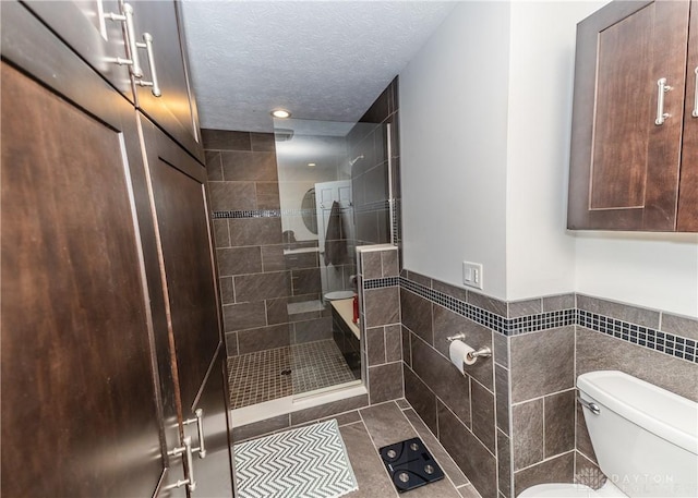 full bath with toilet, tile patterned floors, a tile shower, a textured ceiling, and tile walls