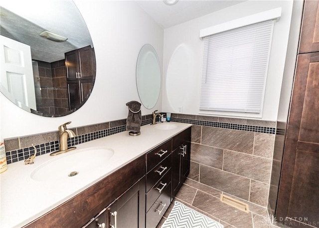 bathroom with visible vents, double vanity, a sink, and tile walls