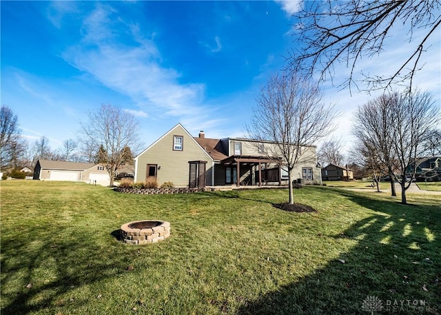 rear view of property featuring a garage, an outdoor fire pit, a chimney, and a lawn